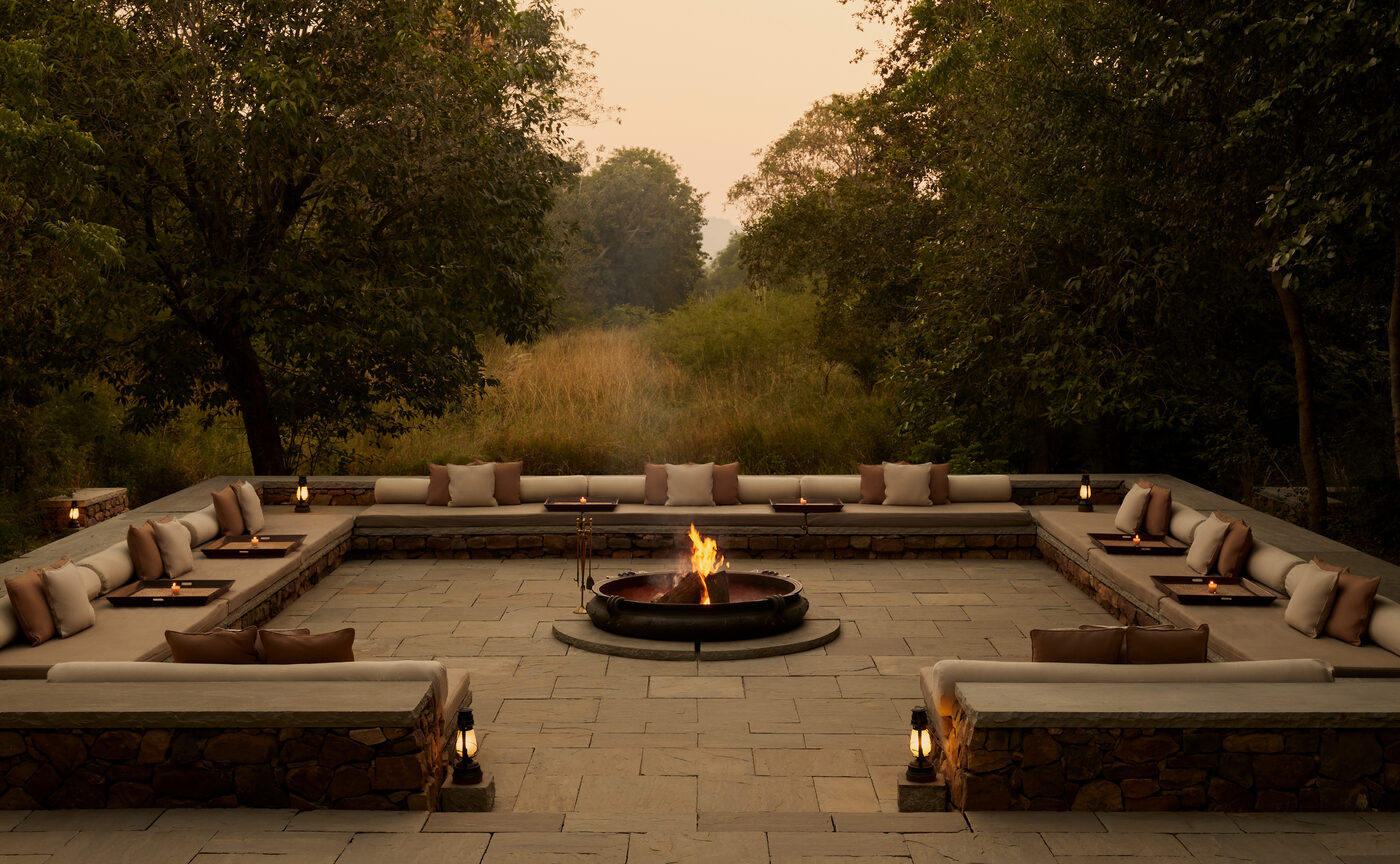 Symmetrical dining pavilion at Aman-i-Kh&aacute;s with a central fire pit, stone seating and a tree-lined avenue at dusk, Ranthambore, India