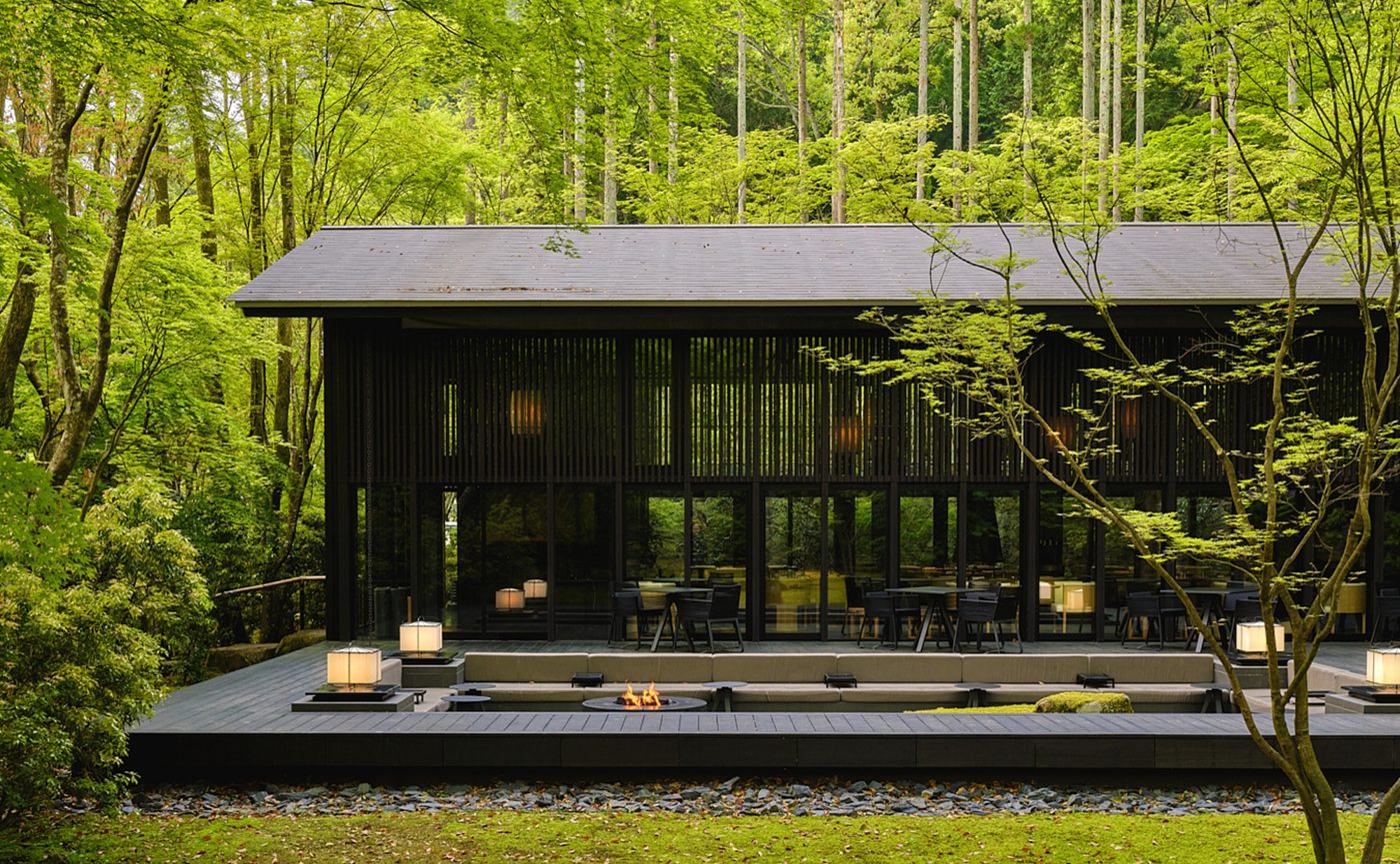 The Living Pavilion by Aman at Aman Kyoto, a dark timber and glass pavilion with a terrace and fire pit set among cedars and maples in the Takagamine forest garden, courtesy of Aman