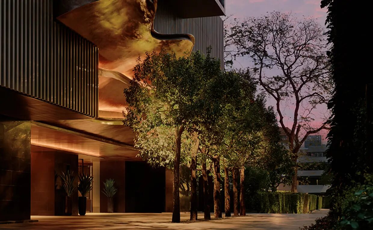 The lit arrival court of Aman Nai Lert Bangkok at dusk, framed by trees in Nai Lert Park