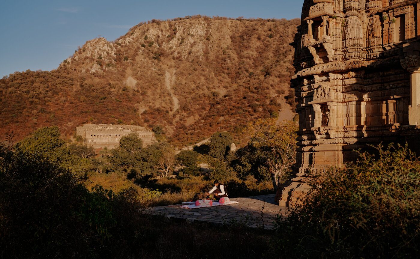 A guest practises yoga at sunrise on a stone terrace at Bhangarh with the Aravalli Hills behind, part of Amanbagh's picnic breakfast, courtesy of Aman