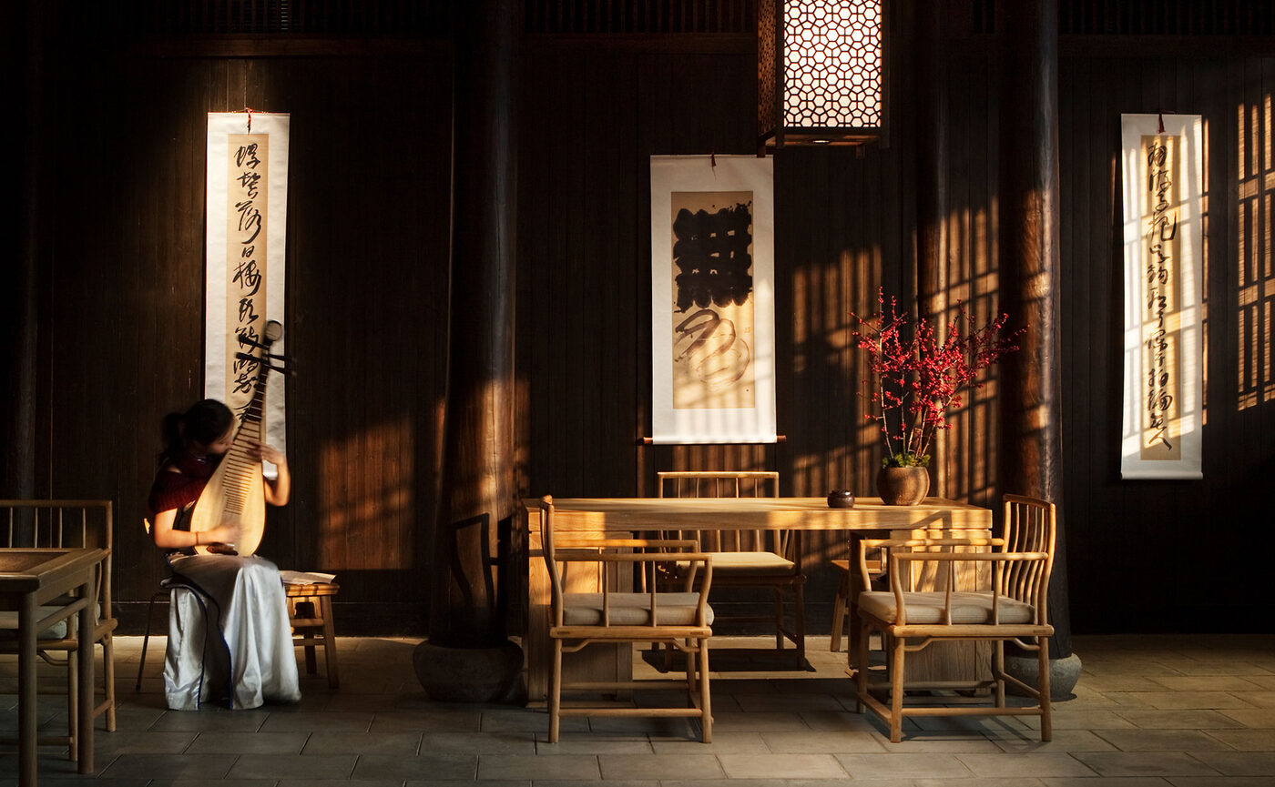 A musician plays the pipa in the main hall of Fayun Place at Amanfayun, afternoon light through the lattice, courtesy of Aman