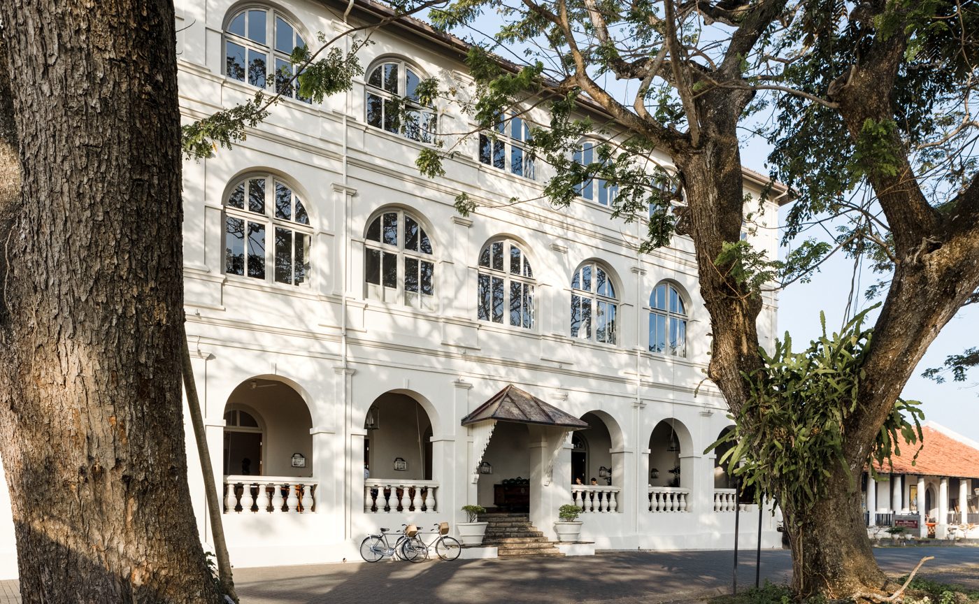The white colonial facade of Amangalla on Church Street inside Galle Fort, with arched windows, a shaded arcaded veranda and bicycles leaning against the wall, courtesy of Aman