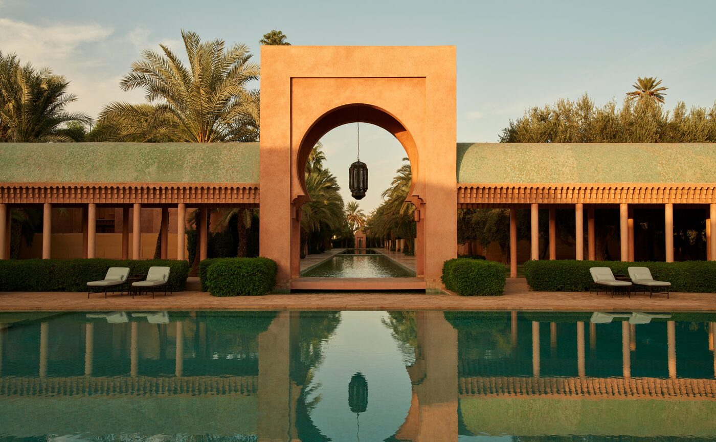 The main pool at Amanjena outside Marrakech, a symmetrical terracotta pavilion with an arched doorway reflected in still turquoise water, courtesy of Aman
