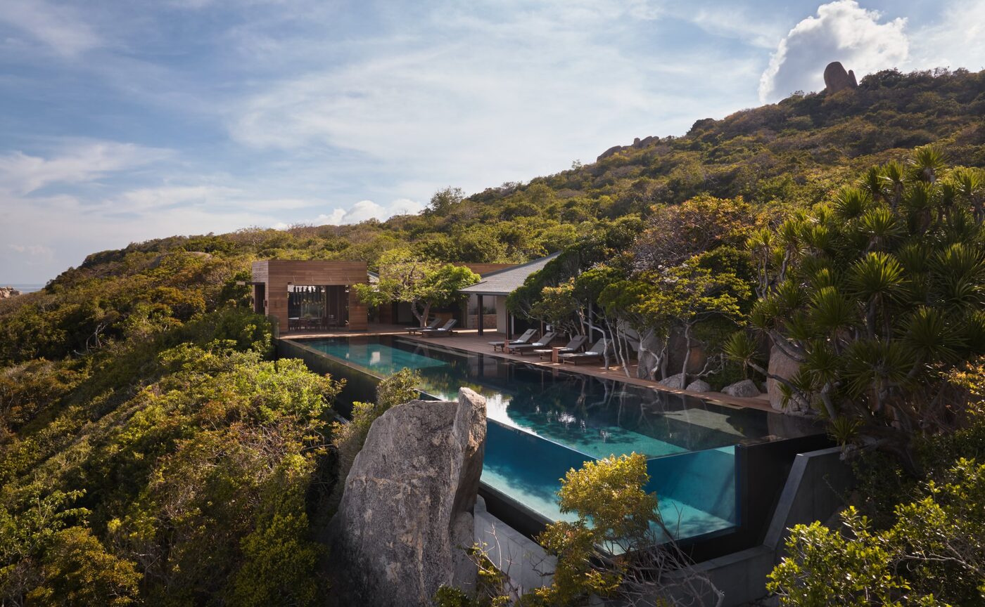 The main pool of the Amanoi Ocean Pool Residence looking out over forested coastline and open sea, Vietnam