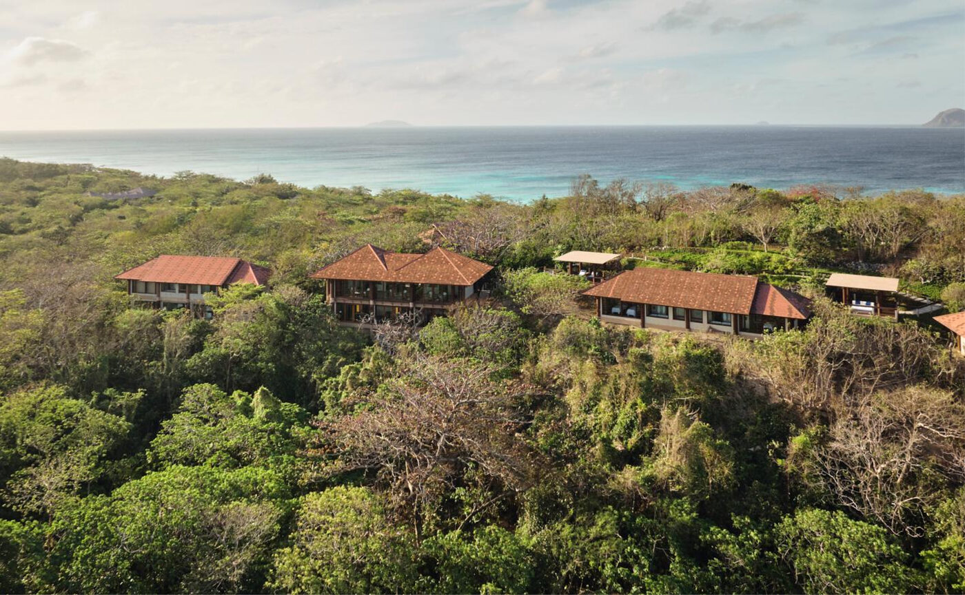 Amanpulo's pavilions set into forested hillside on Pamalican Island, with the sea beyond