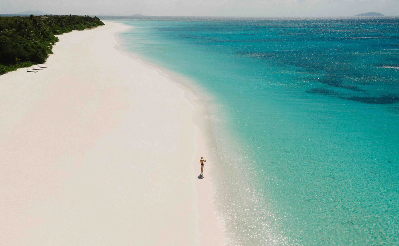 Aerial view of a lone figure on the white sand beach at Amanpulo, with turquoise water off Pamalican Island