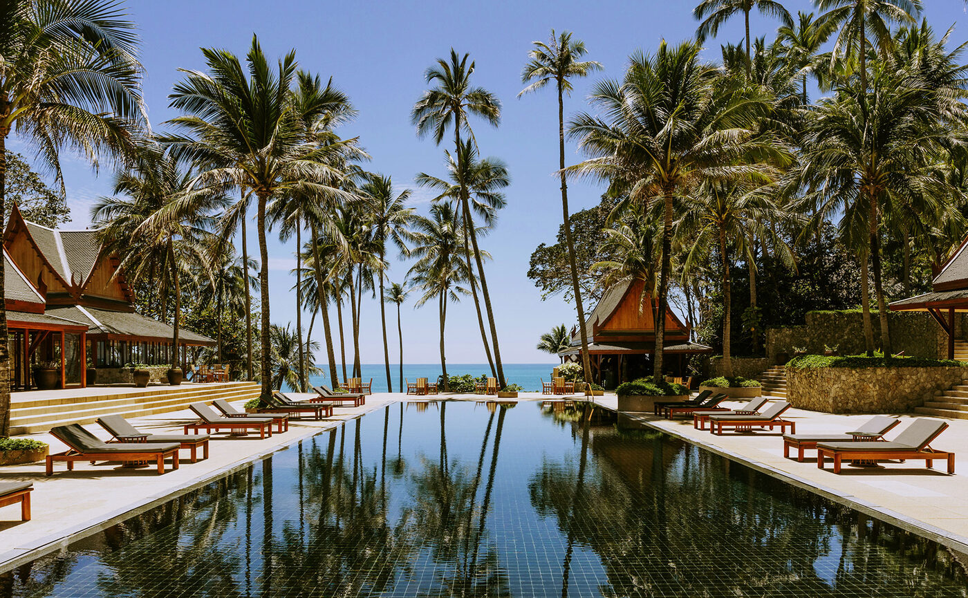 The black-tiled main pool at Amanpuri, Phuket, flanked by twin Thai salas and coconut palms leading to the Andaman Sea