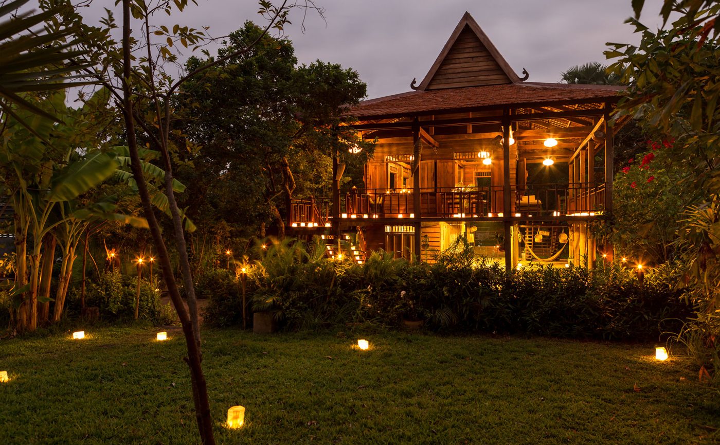 The Khmer Village House, Amansara's stilted timber pavilion inside the Angkor park, lit with candles at dusk, courtesy of Aman