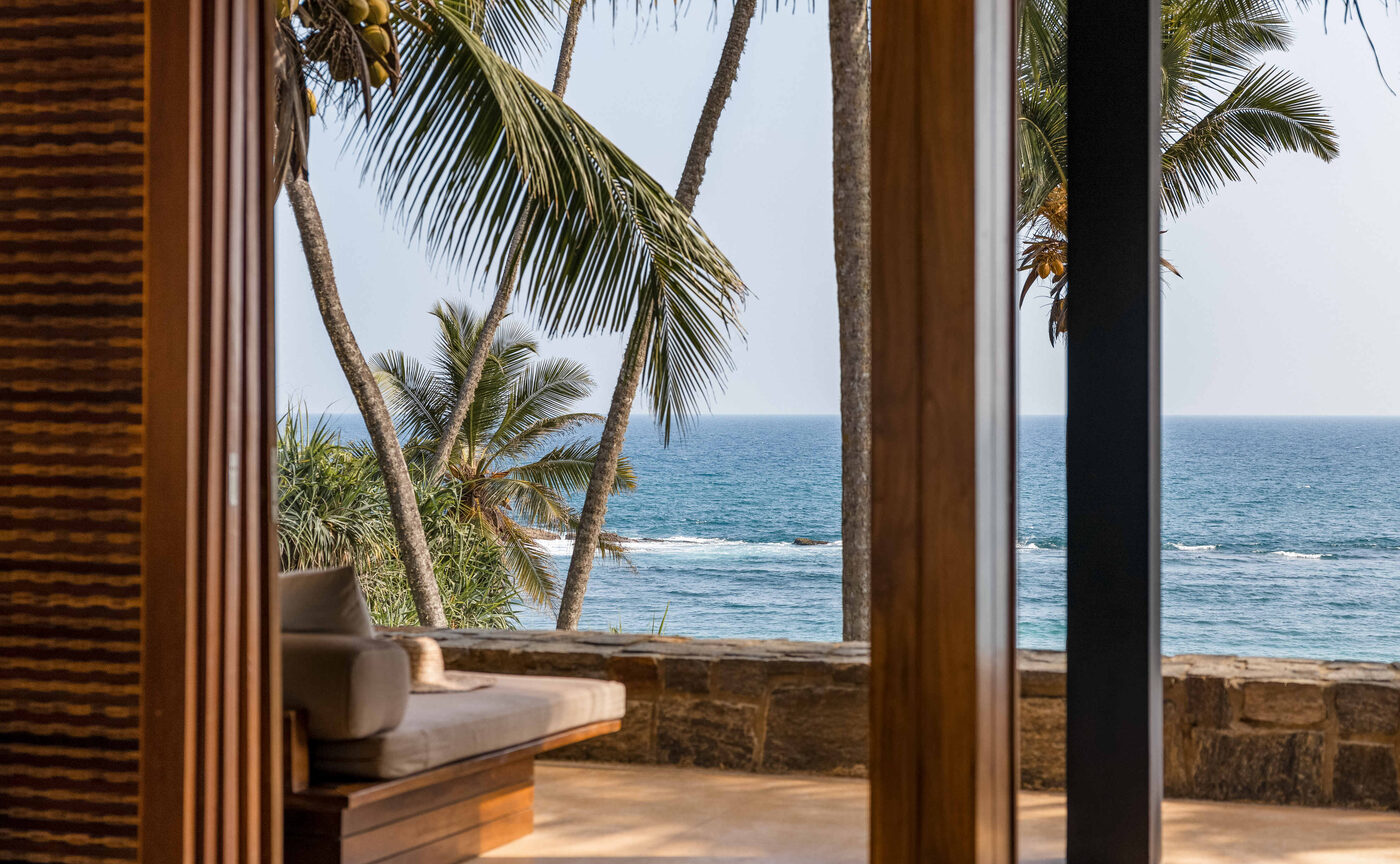Sunbeds and a parasol beneath coconut palms on the sand at Amanwella, Tangalle, Sri Lanka