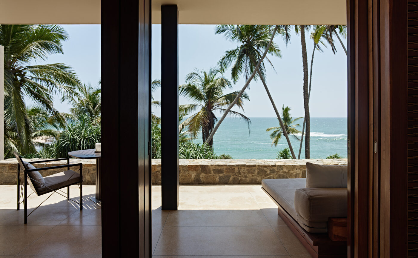 A suite at Amanwella opening through sliding glass doors onto a terrace, palm trees and the Indian Ocean