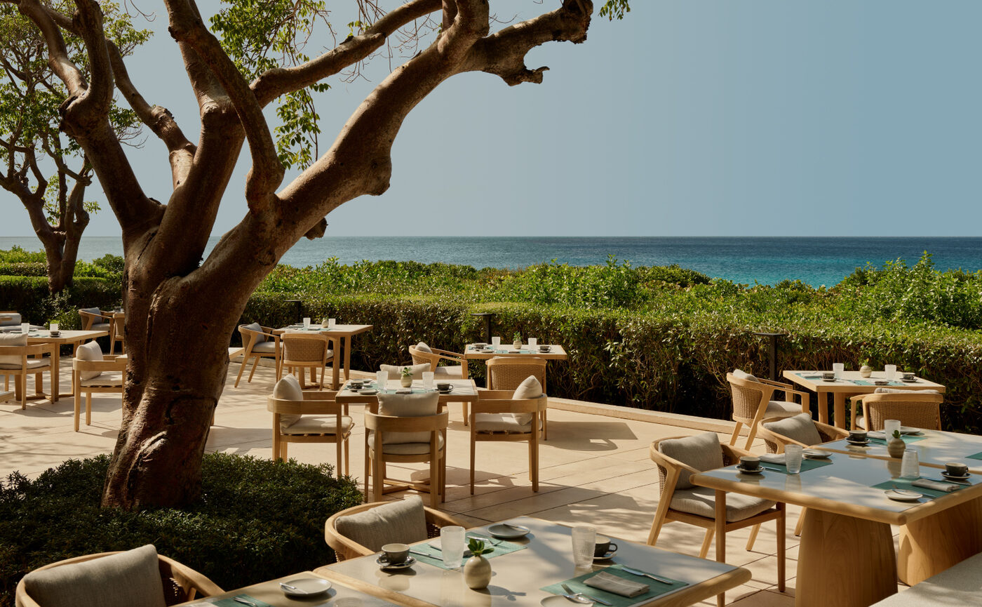 Dining tables beneath a spreading tree at Amanyara's main restaurant, overlooking turquoise water