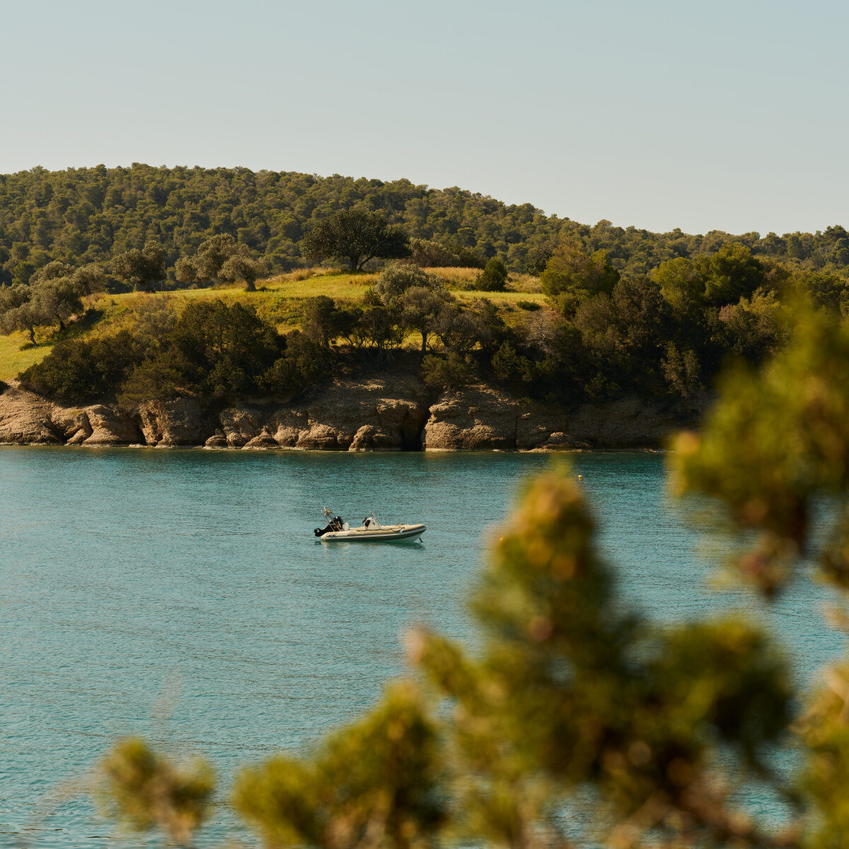 Turquoise water and a golden hillside at the Amanzoe Beach Club, with a boat moored offshore, Porto Heli, Greece