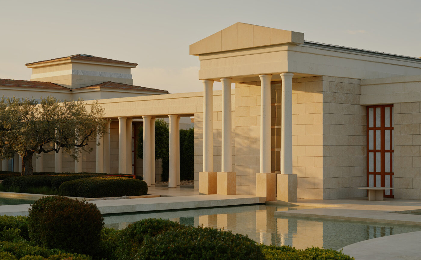 Whitewashed colonnaded pavilions at Amanzoe reflected in still water at dusk, Porto Heli, Greece