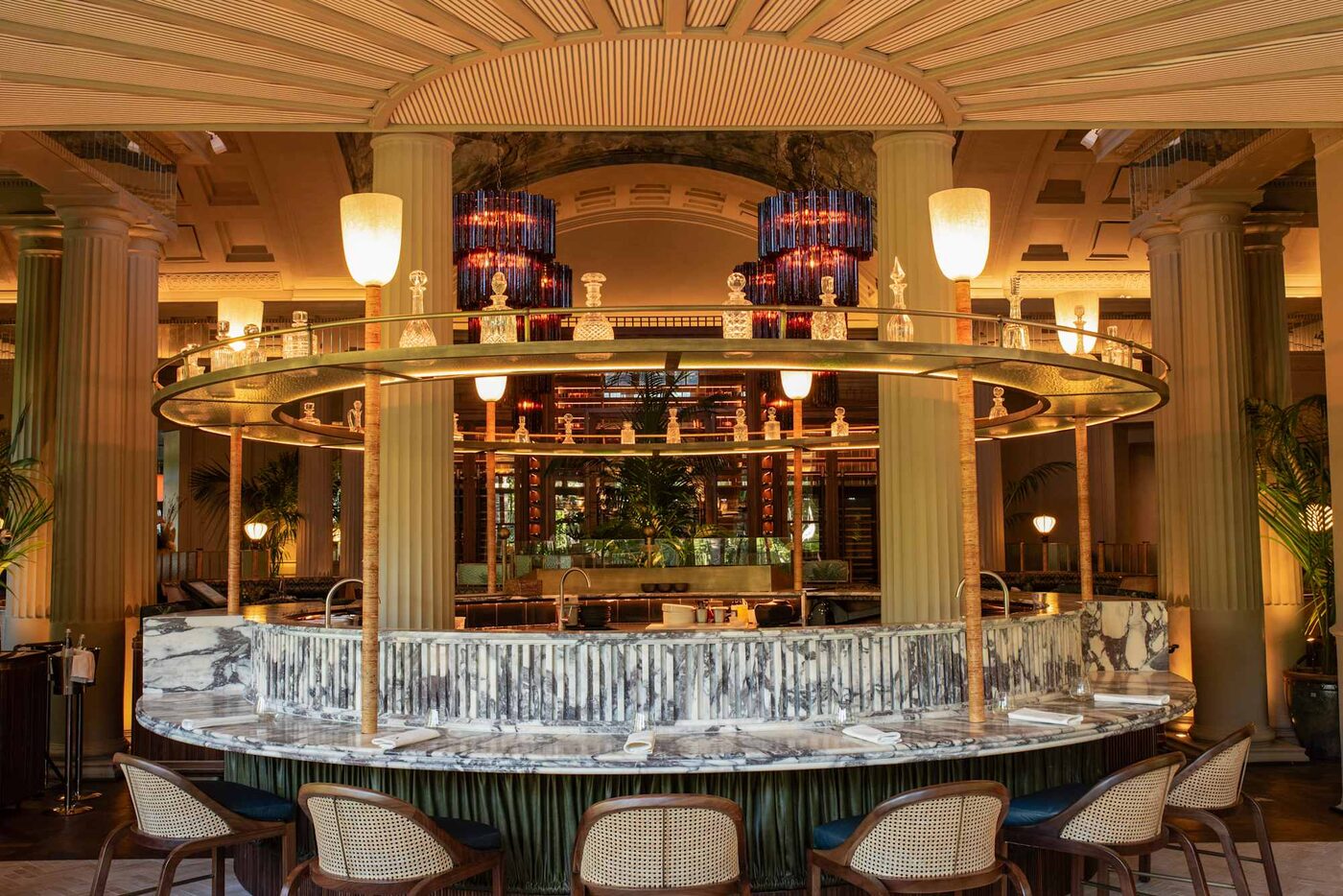 The circular marble bar at Amura by Angel Leon, Mount Nelson, A Belmond Hotel, Cape Town, ringed with decanters beneath tiered glass chandeliers