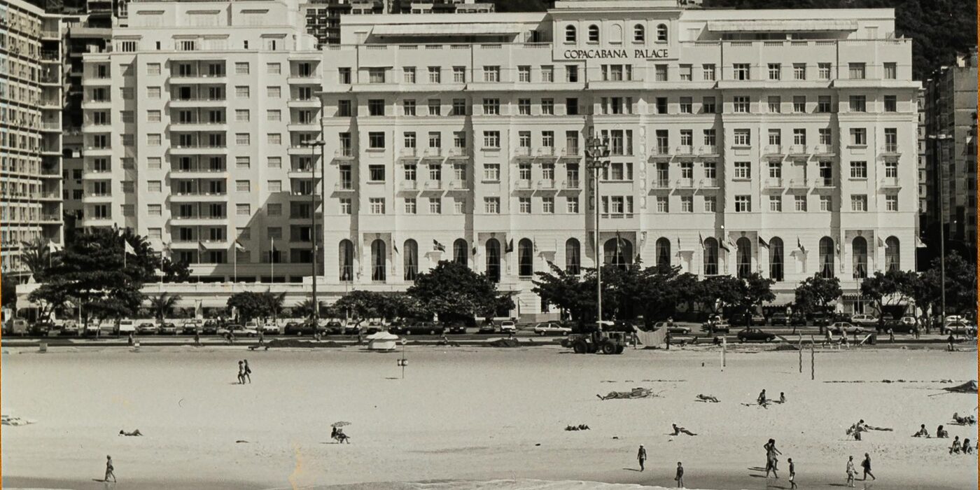 Archive photograph of the white facade of Copacabana Palace on Avenida Atlantica, Rio de Janeiro, with bathers on Copacabana Beach in front of it, courtesy of Belmond