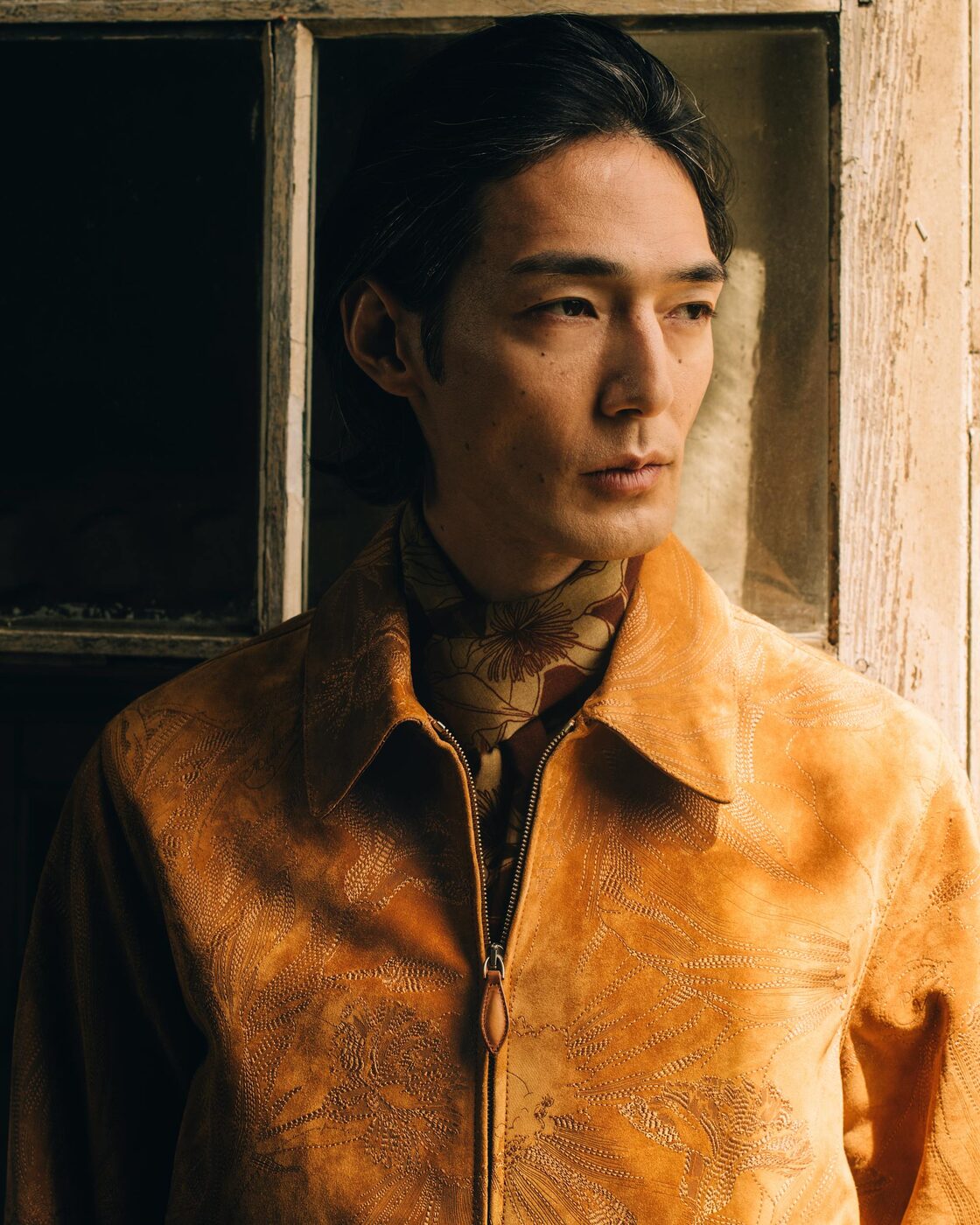 A model in a golden suede Berluti blouson engraved with a flower pattern, worn over a printed scarf, from the Spring-Summer 2027 lookbook