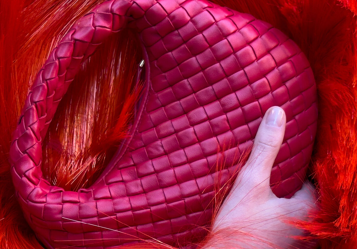 Close detail of the woven intrecciato leather on a red Bottega Veneta bag held in one hand
