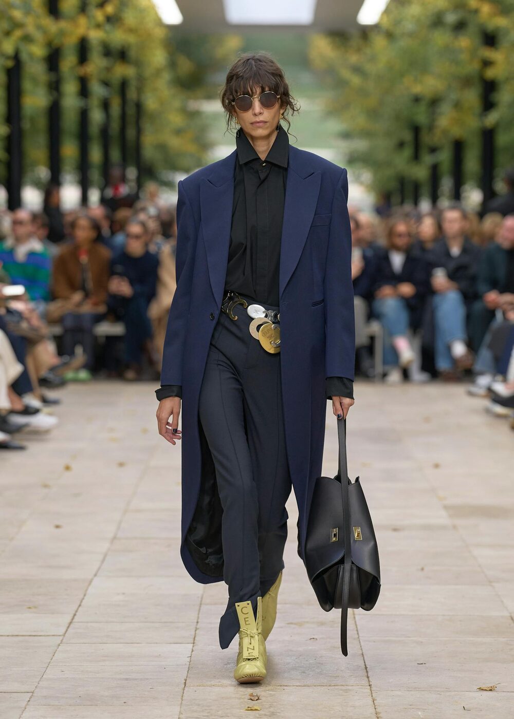 A Celine Summer 2026 look under Michael Rider, a navy coat over tailoring with a New Luggage tote and logo boots