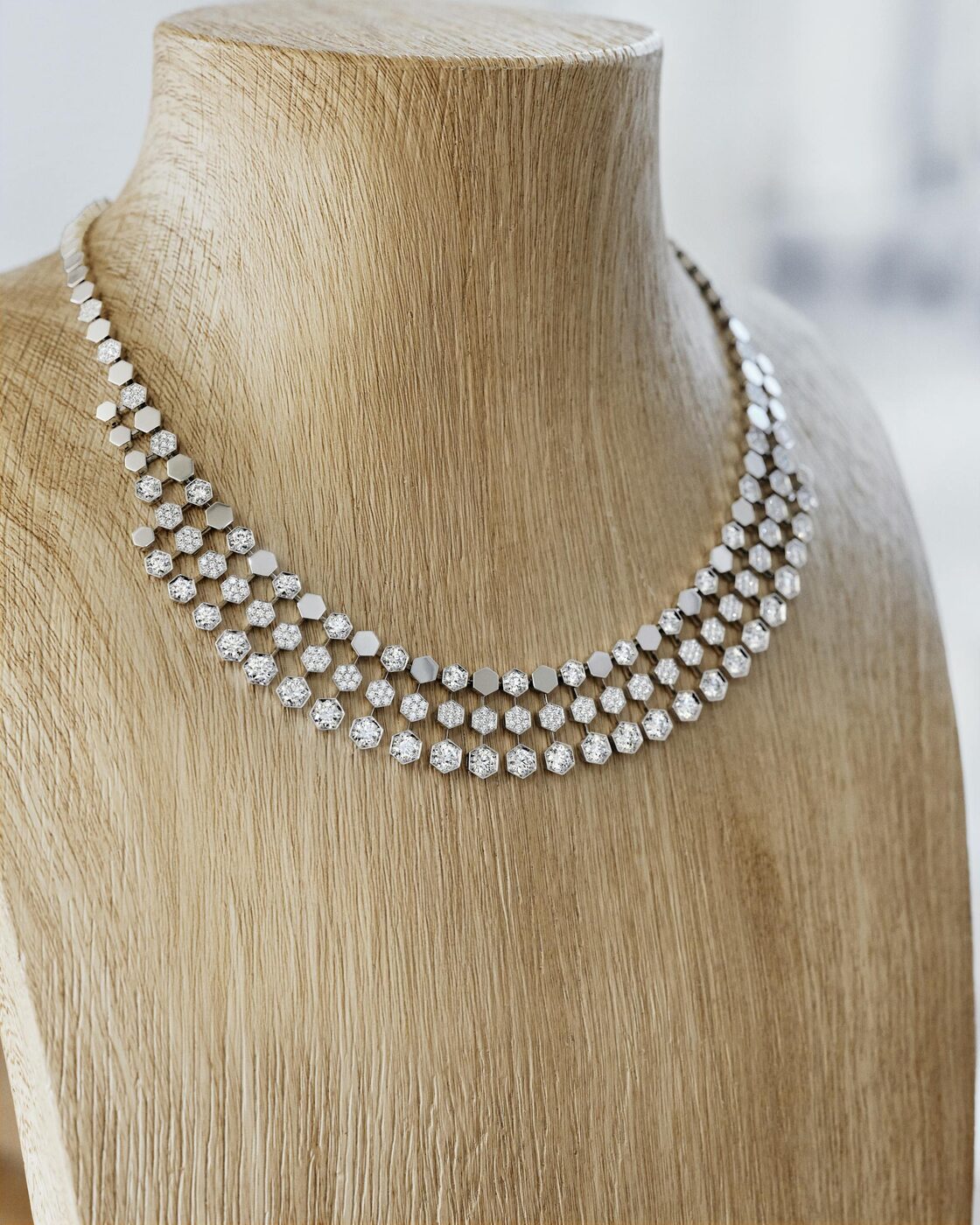 A Bee de Chaumet High Jewelry necklace in polished gold and diamonds, its honeycomb motif set against a pale background