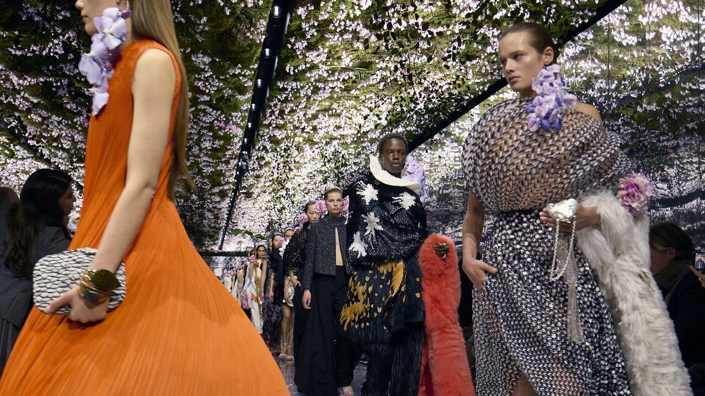 Models walking the Dior Fall Winter 2026 haute couture show under a flowering canopy at the Musee Rodin, in pleated and metallic looks