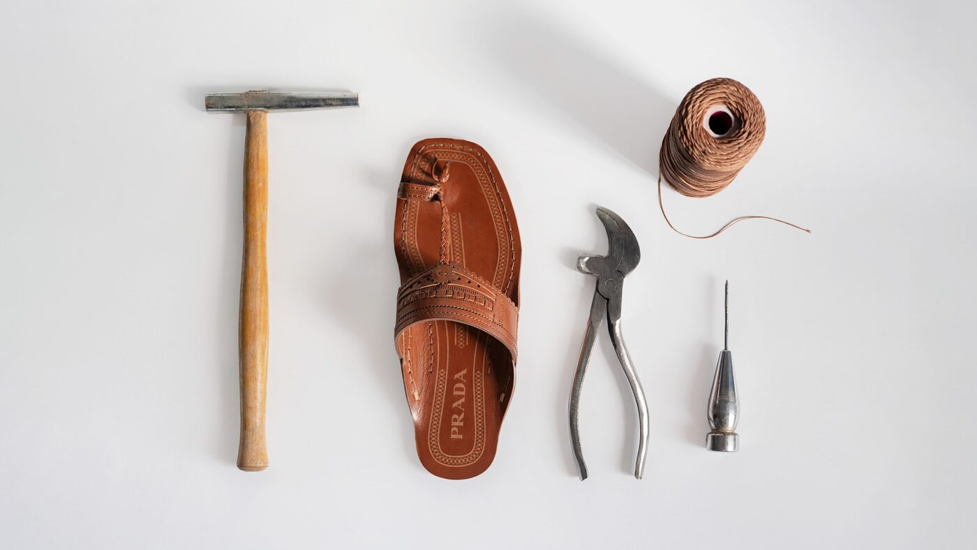 A Prada Kolhapuri sandal laid out with a cobbler's hammer, pliers, awl and thread