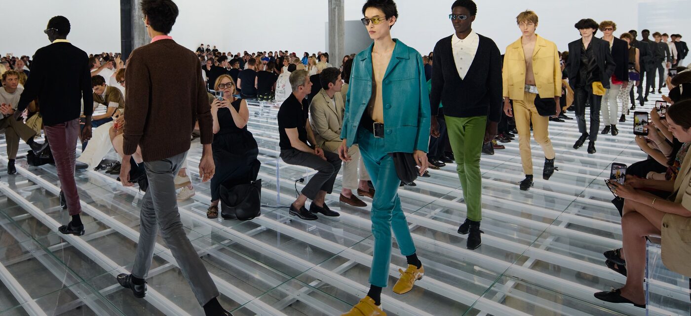 Prada Spring/Summer 2027 men's runway on a clear Perspex floor at Fondazione Prada, close-cut tailoring in turquoise, yellow and green