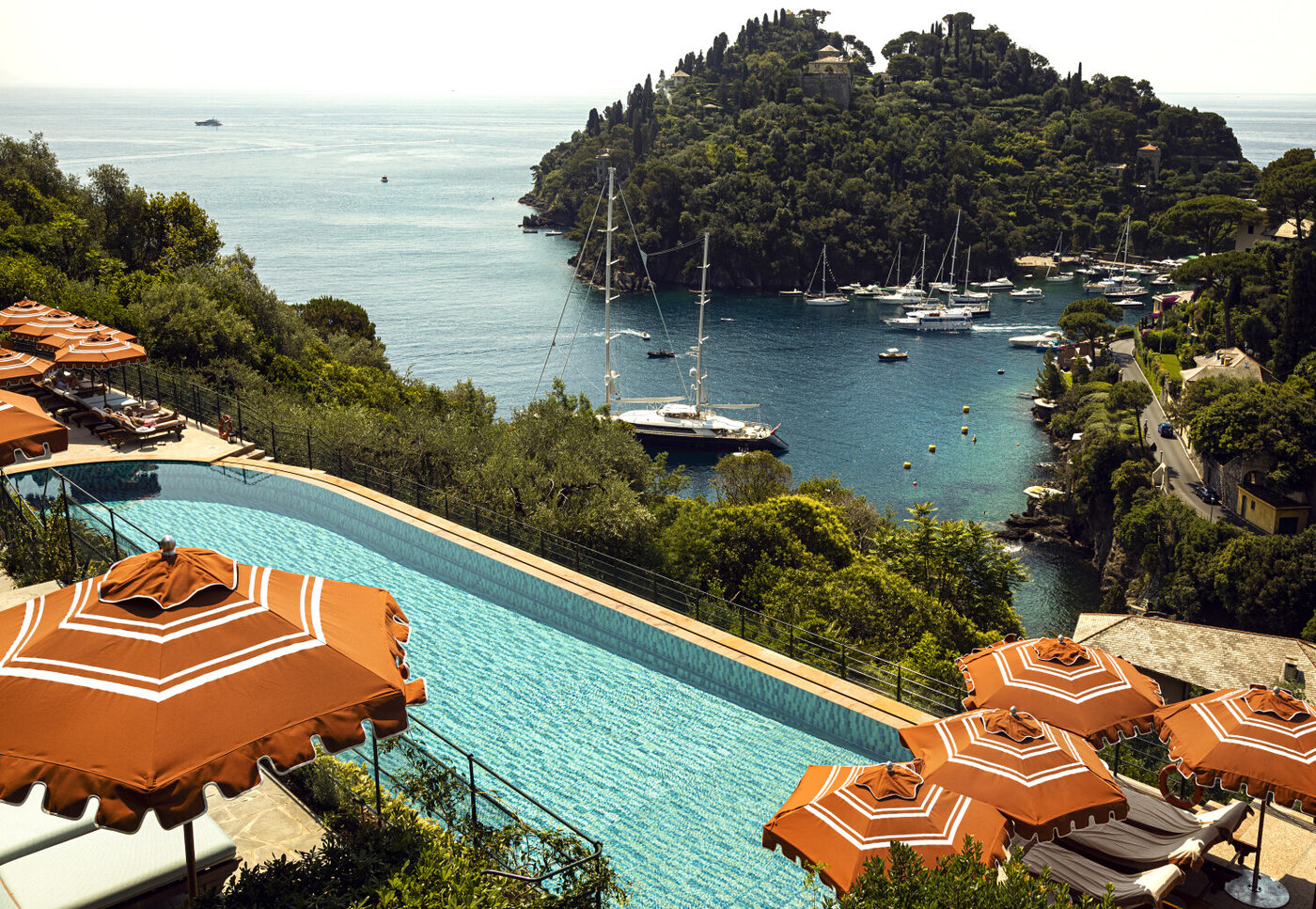 The pool terrace at Splendido, A Belmond Hotel, Portofino, lined with orange parasols above the harbour and wooded promontory