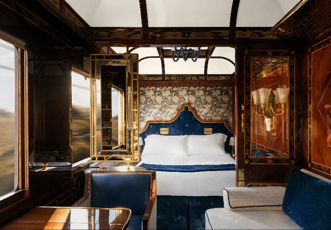 A Grand Suite aboard the Venice Simplon-Orient-Express, with blue velvet upholstery, inlaid wood panelling, gilt mirrors and the landscape blurring past the window, courtesy of Belmond